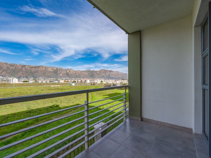 A clean, covered balcony featuring tiled flooring and a metal balustrade, offering expansive views of the surrounding landscape and mountains.
