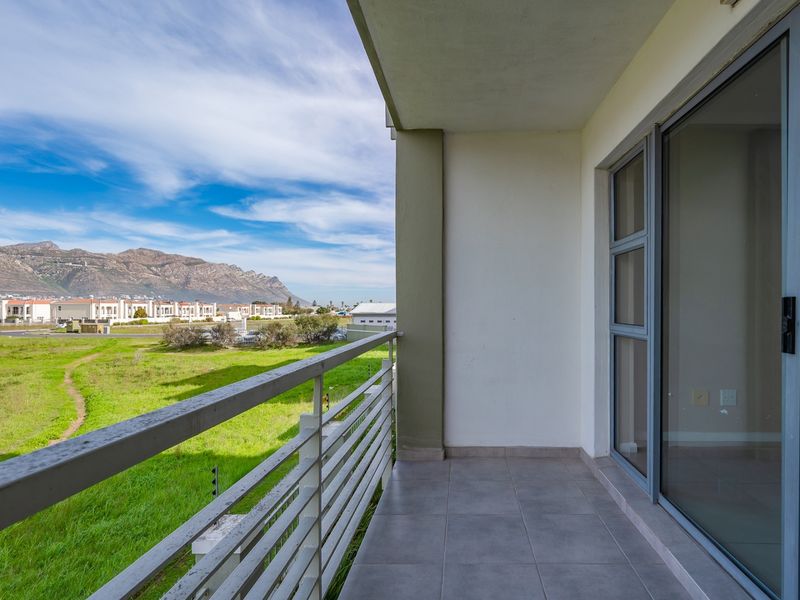 A clean, tiled balcony featuring a metal balustrade and sliding glass door access, offering scenic mountain and landscape views.