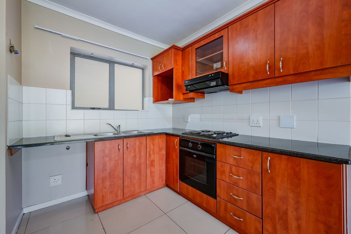 A functional kitchen featuring wooden cabinetry, granite countertops, a built-in oven with gas hob, and tiled finishes throughout.