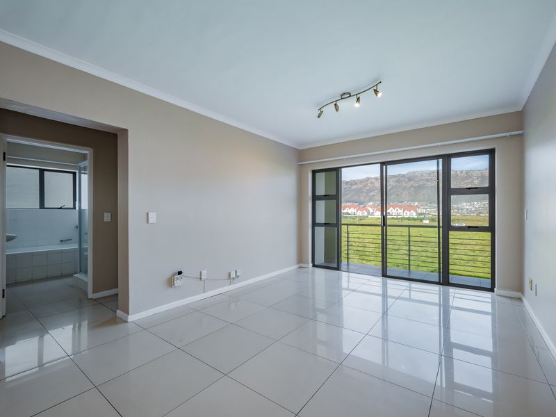 Spacious, light-filled living area featuring polished tile floors, modern track lighting, and large sliding doors opening to a balcony with scenic mountain views.