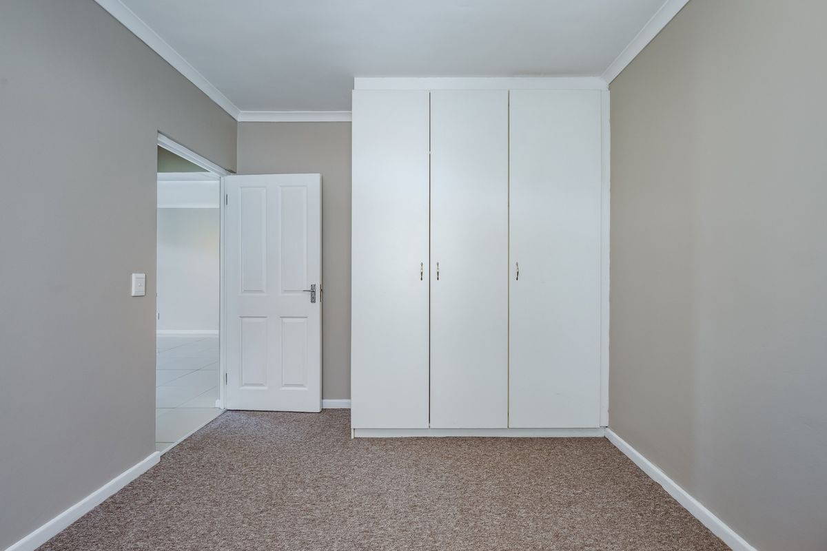 A clean, empty bedroom featuring neutral wall tones, fitted carpet flooring, and a white built-in wardrobe with ample storage space.