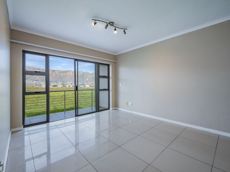 A bright, empty living room featuring large sliding glass doors that open to a balcony with scenic mountain and landscape views.