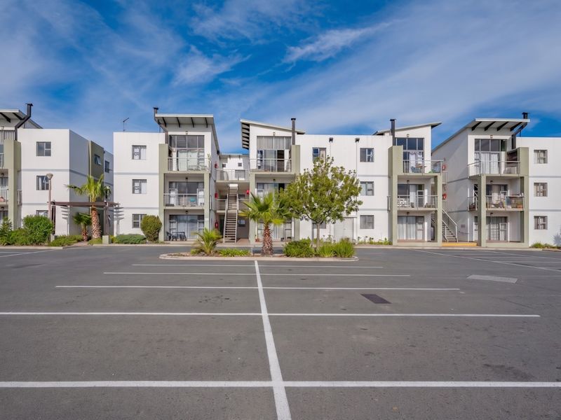 A clear front view of a modern multi-story apartment complex featuring paved parking, balconies, and well-maintained exterior facades.