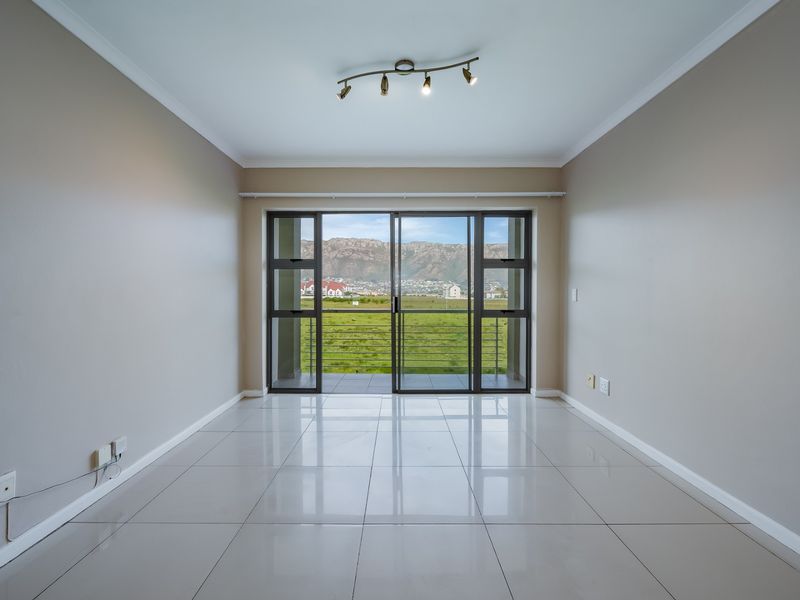 An empty, well-maintained living room featuring polished tile floors, modern track lighting, and a large sliding glass door opening to a scenic mountain view.