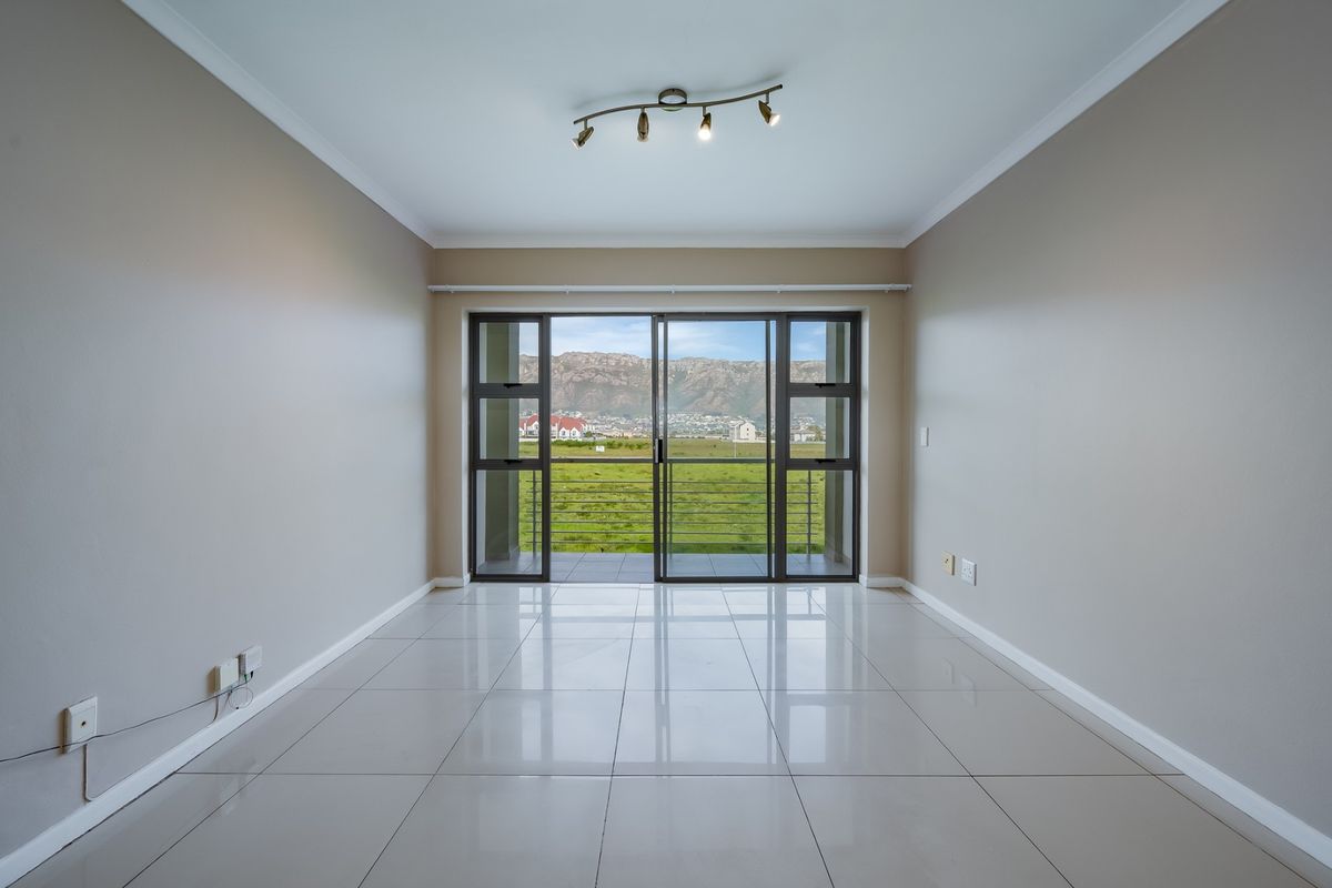 An empty, well-maintained living room featuring polished tile floors, modern track lighting, and a large sliding glass door opening to a scenic mountain view.