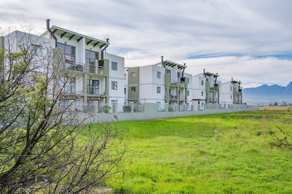 A view of the rear elevation of a modern apartment complex featuring multiple levels with balconies and perimeter fencing.