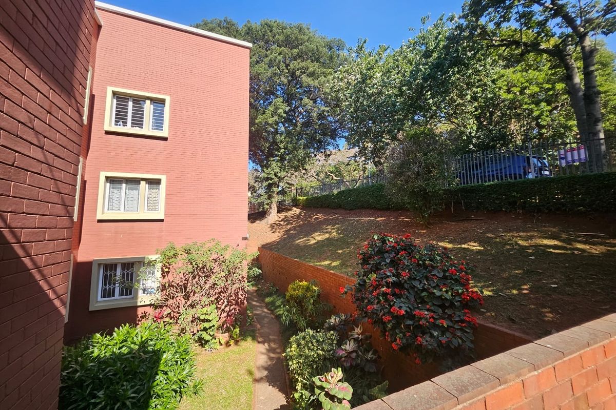 Rear exterior view of the apartment building featuring a brick facade, security-fitted windows, and a well-maintained terraced garden area.