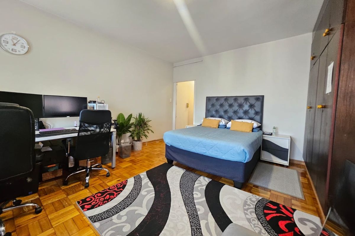 Spacious bedroom featuring classic parquet flooring and extensive built-in cupboard storage, offering a functional layout with ample space for a home office setup.