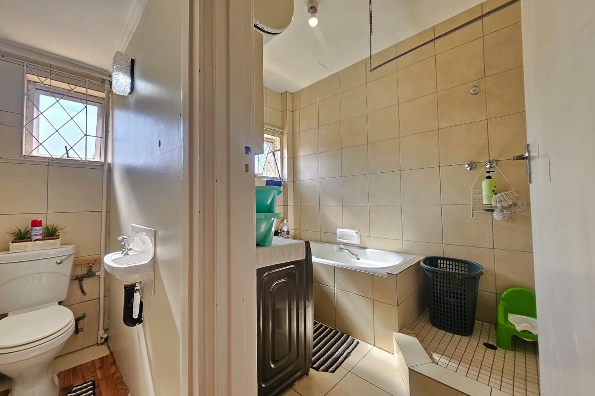 A dated bathroom featuring a built-in bathtub, separate shower area, wall-mounted basin, and toilet, with tiled finishes throughout.
