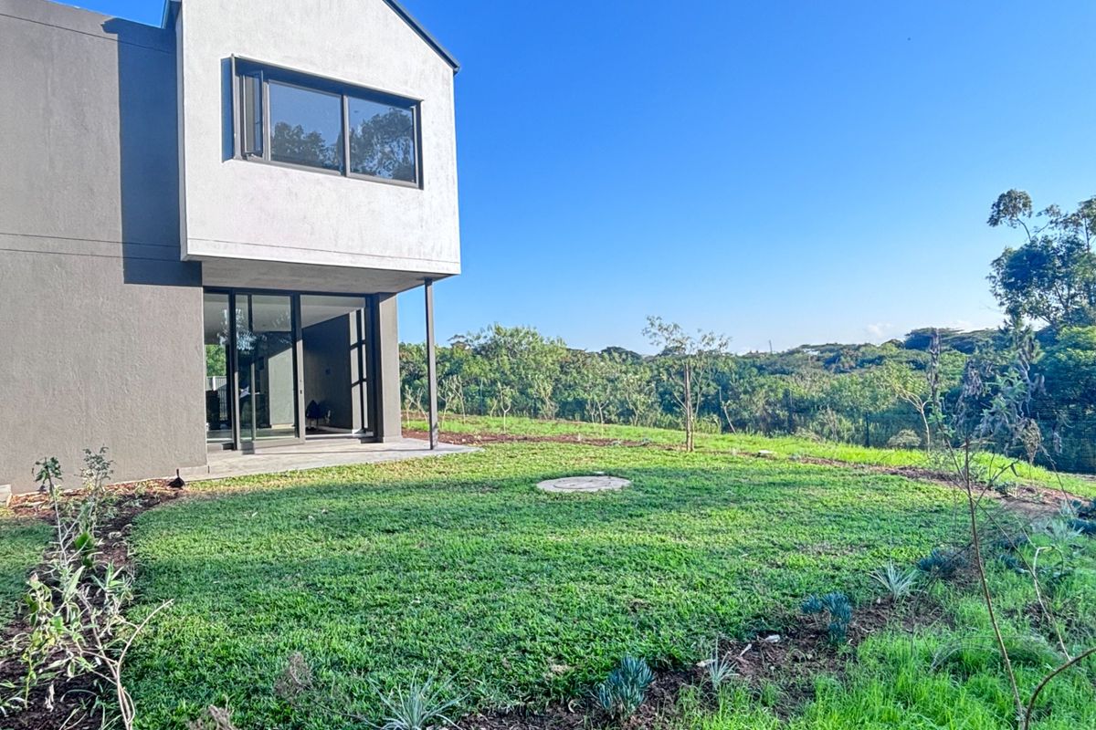 Rear view of the townhouse featuring a modern facade, sliding glass doors leading to a patio, and a spacious private garden area.