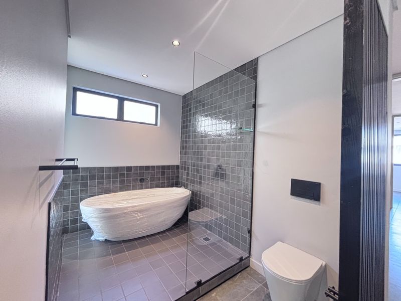 Modern bathroom featuring a freestanding bathtub, glass-enclosed shower area, wall-mounted toilet, and contemporary grey tiled finishes.