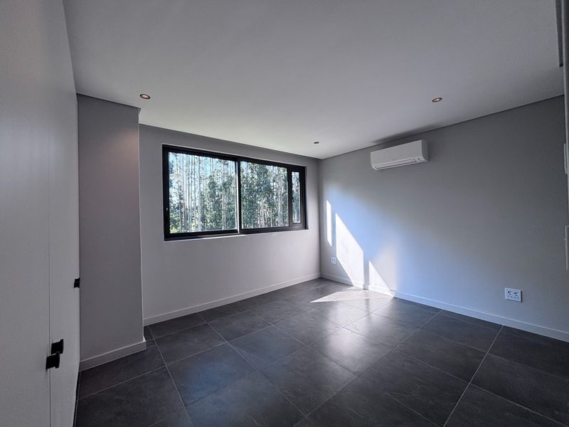 A bright, modern, and empty bedroom featuring dark tiled flooring, built-in cupboards, recessed lighting, and a wall-mounted air conditioning unit.