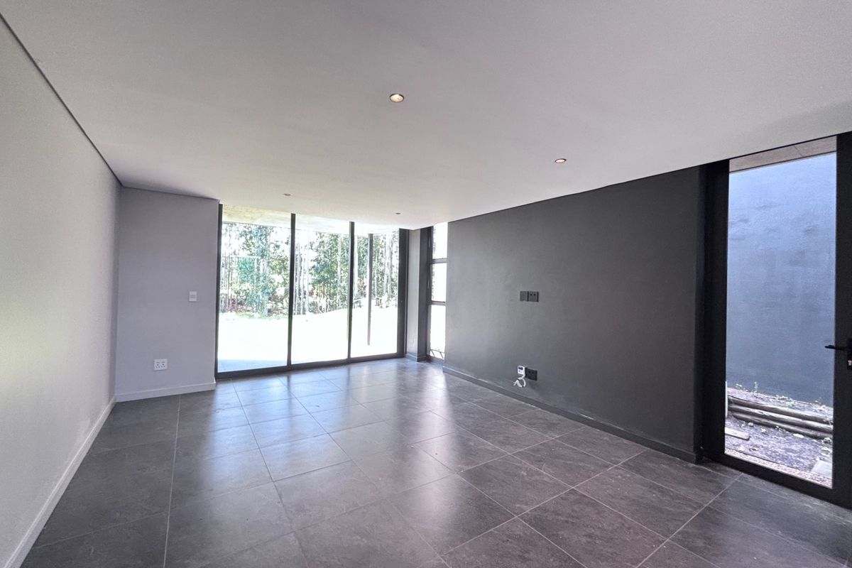 A modern, empty living area featuring large format floor tiles, recessed downlights, a striking black feature wall, and expansive sliding glass doors leading outdoors.