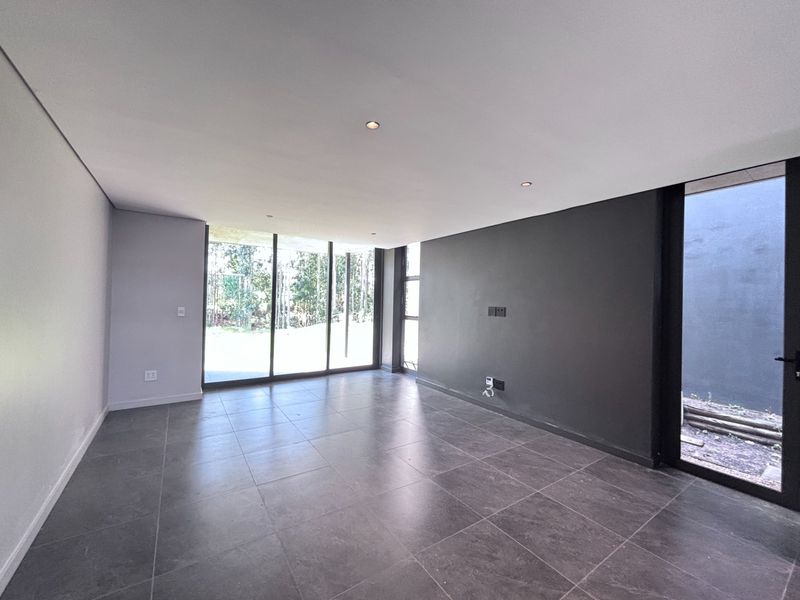 A modern, empty living area featuring large format floor tiles, recessed downlights, a striking black feature wall, and expansive sliding glass doors leading outdoors.