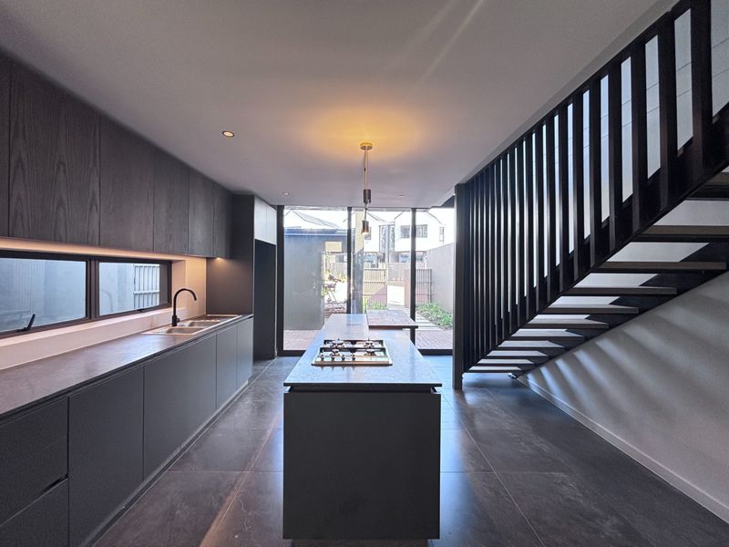 Modern open-plan kitchen featuring dark cabinetry, a central island with a built-in gas cooktop, tiled flooring, and direct access to the rear patio.
