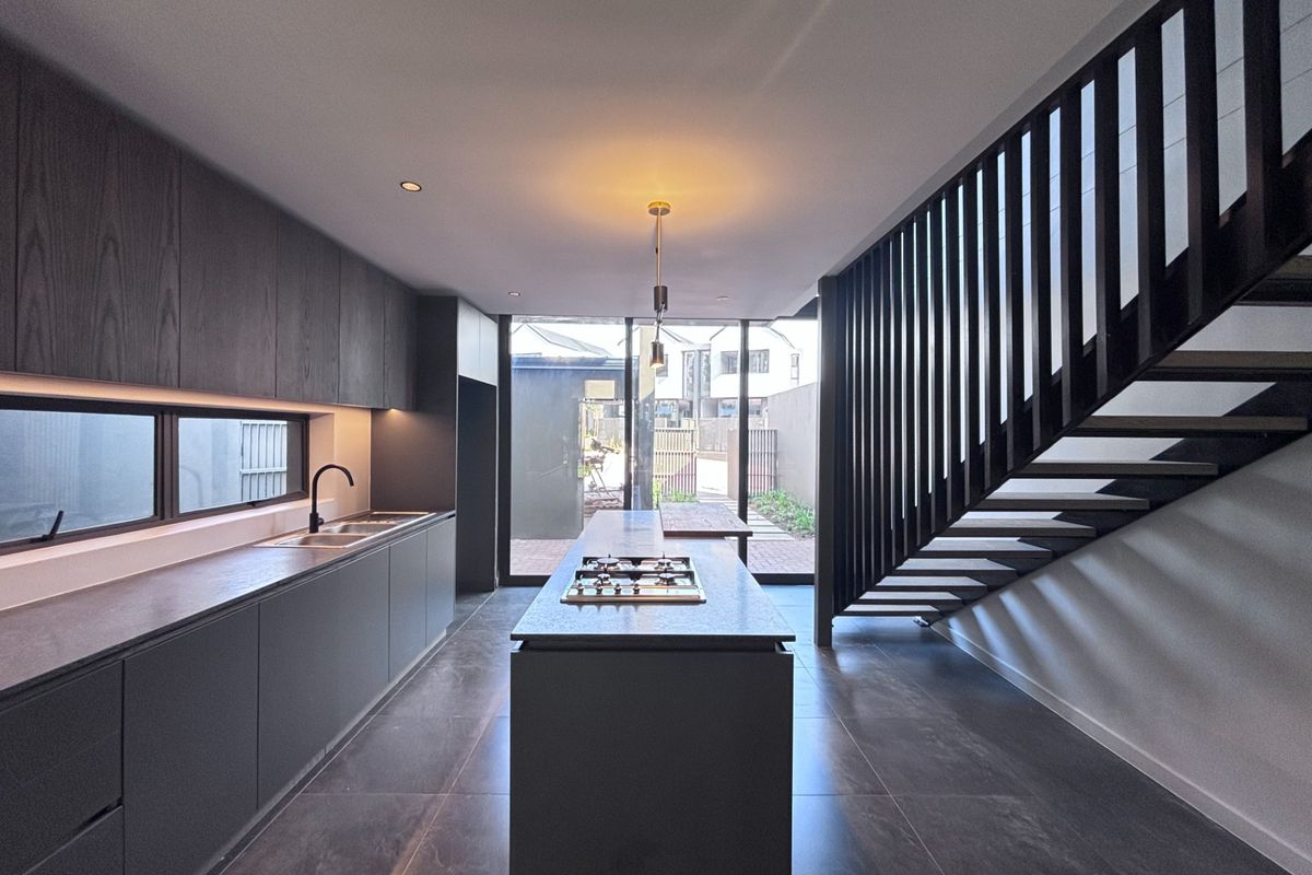 Modern open-plan kitchen featuring dark cabinetry, a central island with a built-in gas cooktop, tiled flooring, and direct access to the rear patio.