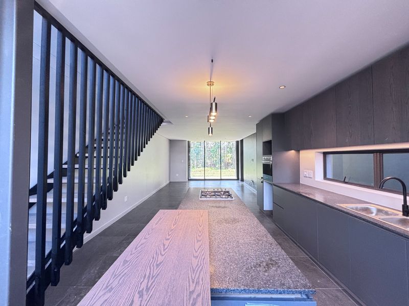 Modern open-plan kitchen featuring a large island with gas hob, dark cabinetry, stone countertops, and a striking staircase with a vertical balustrade.