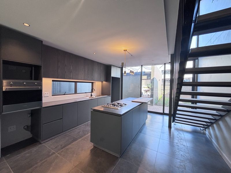 Modern open-plan kitchen featuring dark cabinetry, stone countertops, a central island with a gas hob, and direct access to the outdoor area.