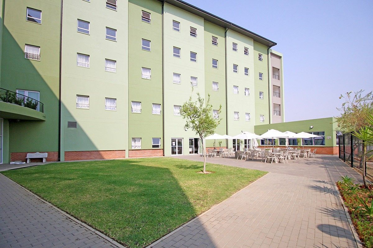 Rear exterior view of the retirement village building featuring a paved courtyard area, landscaped lawn, and multi-story facade.