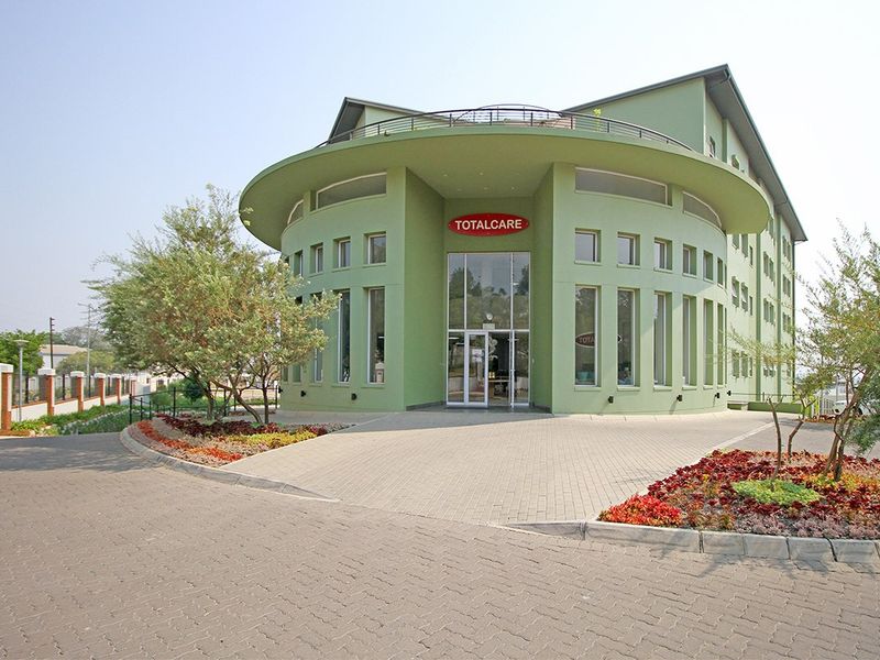 Front exterior view of a modern retirement village facility featuring a distinctive curved facade, paved driveway, and landscaped garden beds.