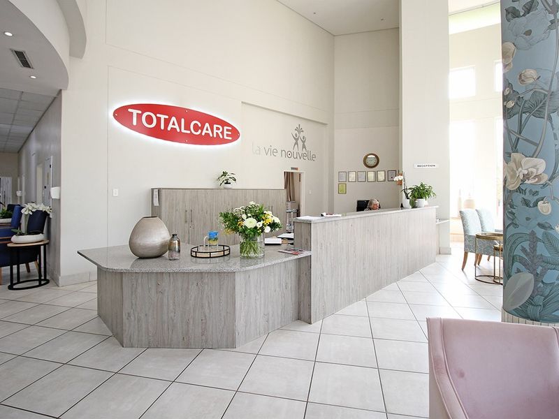 A bright and modern retirement village reception area featuring a large service desk, high ceilings, and neutral tiled flooring.