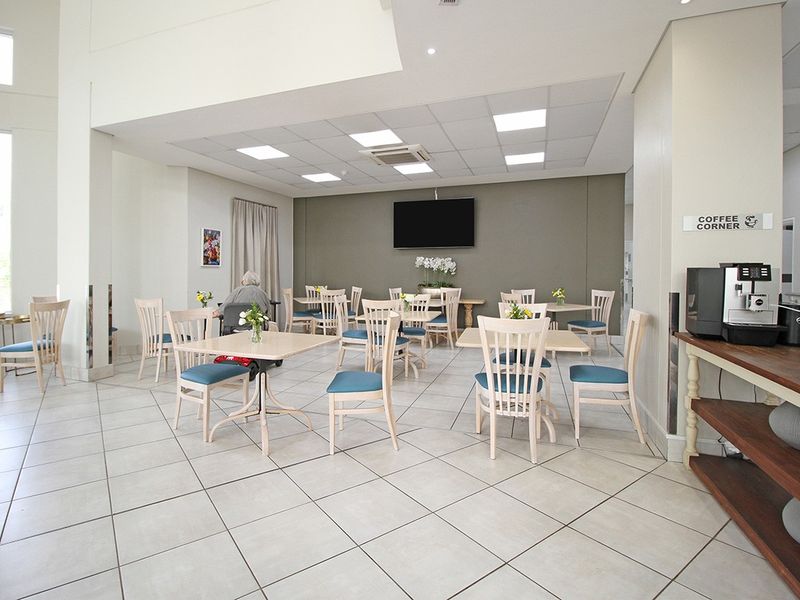 A bright and spacious communal clubhouse area featuring tiled flooring, recessed lighting, and a dedicated coffee corner for residents.