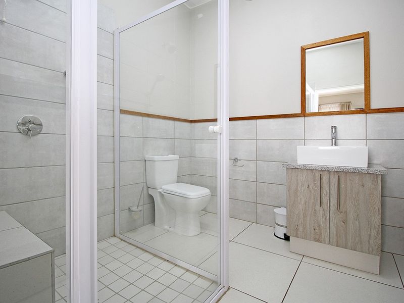 A clean and modern bathroom featuring a walk-in shower with glass screen, a vanity unit with vessel sink, and neutral wall tiling.