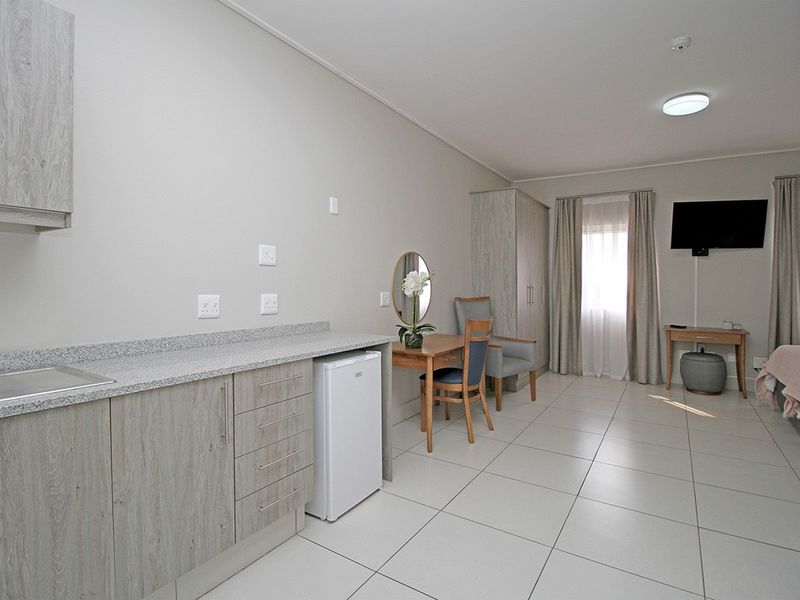 A well-maintained open-plan living space featuring modern light wood-grain cabinetry, stone-look countertops, and neutral ceramic floor tiles.