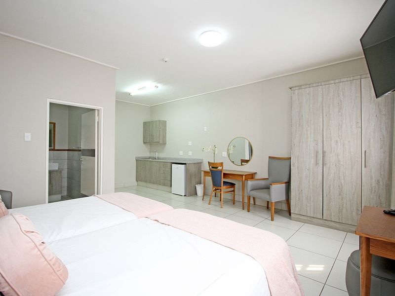 Spacious bedroom featuring a built-in wardrobe, kitchenette area with sink, and direct access to an en-suite bathroom with tiled flooring throughout.