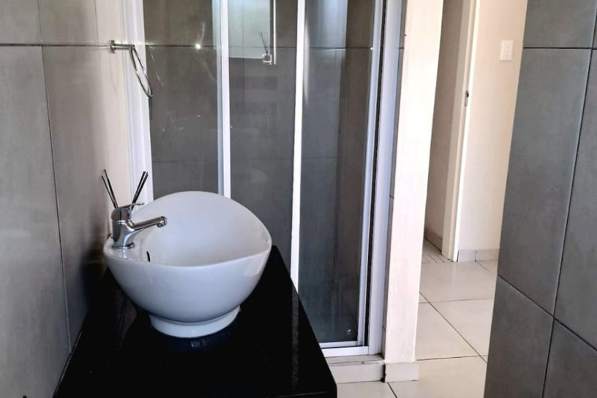 A modern bathroom featuring a vessel sink on a vanity cabinet, a glass-enclosed shower, and neutral wall and floor tiling.
