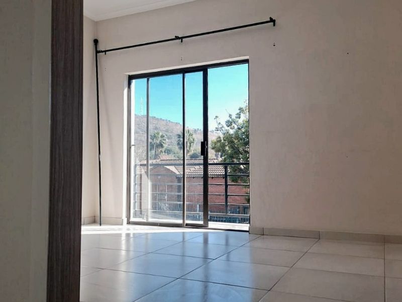 An empty, well-lit living area featuring neutral tiled flooring and a sliding glass door that opens onto a balcony.