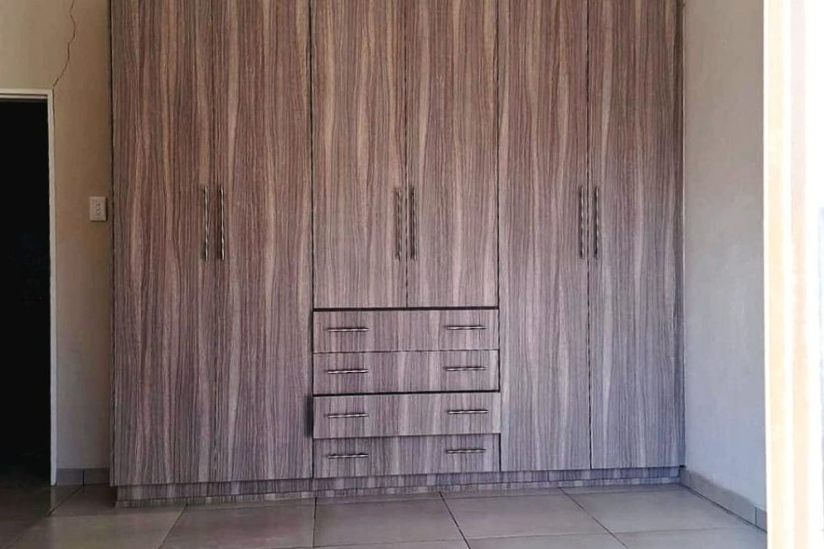 A bedroom featuring large wood-grain built-in cupboards, neutral tiled flooring, and recessed lighting. The room is vacant and ready for personalization.