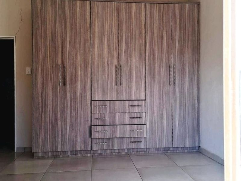 A bedroom featuring large wood-grain built-in cupboards, neutral tiled flooring, and recessed lighting. The room is vacant and ready for personalization.
