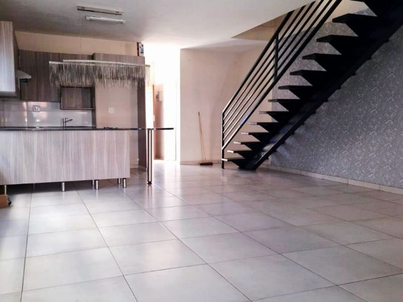 Spacious open-plan living area featuring a modern kitchen with island, tiled flooring, and a striking staircase leading to the upper level.