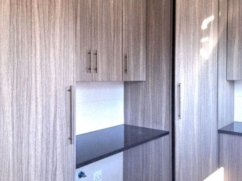 A functional laundry area featuring modern wood-grain cabinetry, dark laminate countertops, and dedicated plumbing connections for appliances.
