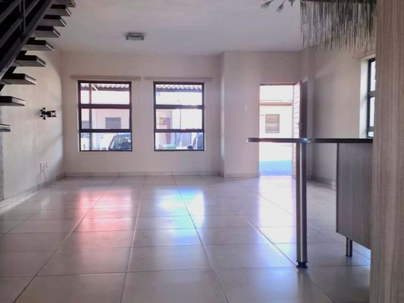 Spacious open-plan living area featuring tiled flooring, a built-in breakfast bar, and a modern staircase leading to the upper level.