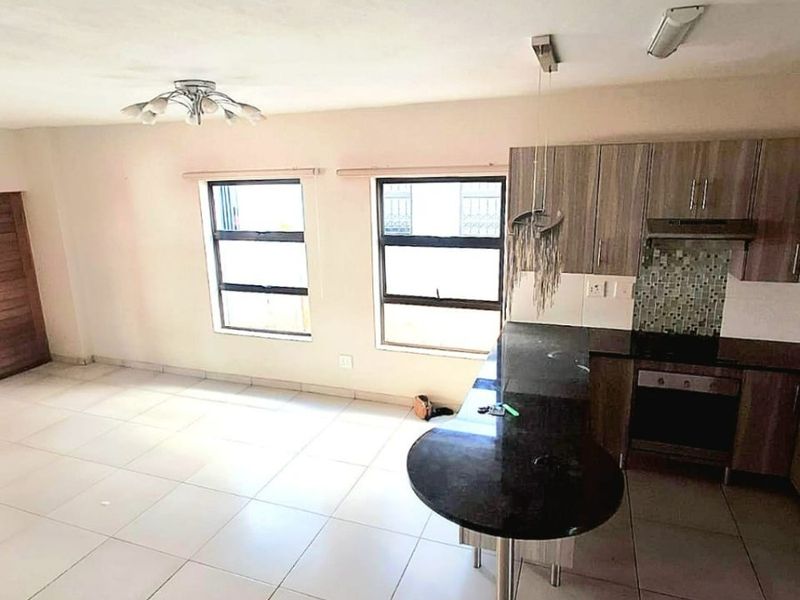 Open-plan living area featuring a modern kitchen with granite countertops, breakfast bar, built-in oven, hob, and tiled flooring throughout.
