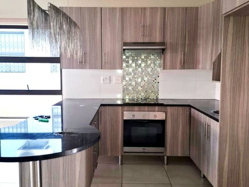 Modern kitchen featuring wood-grain cabinetry, granite countertops, a breakfast bar, and built-in appliances including an oven and extractor fan.