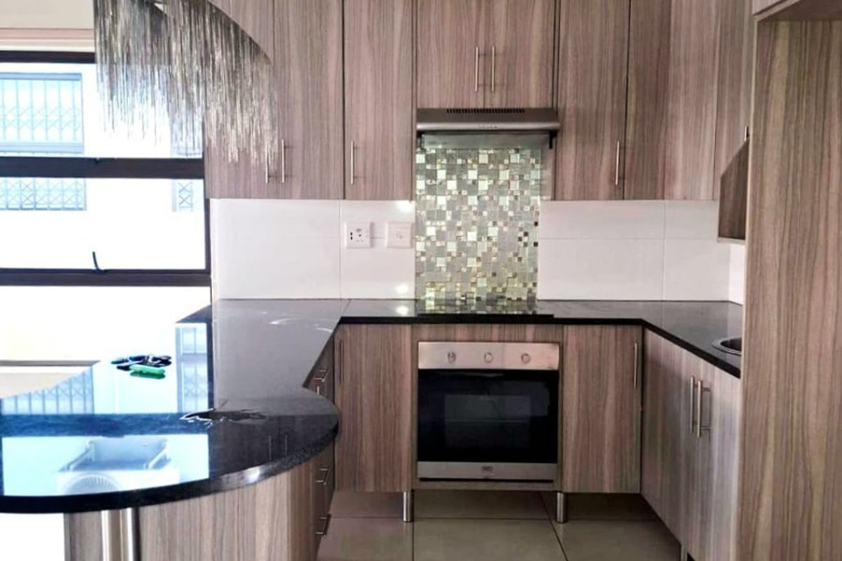 Modern kitchen featuring wood-grain cabinetry, granite countertops, a breakfast bar, and built-in appliances including an oven and extractor fan.
