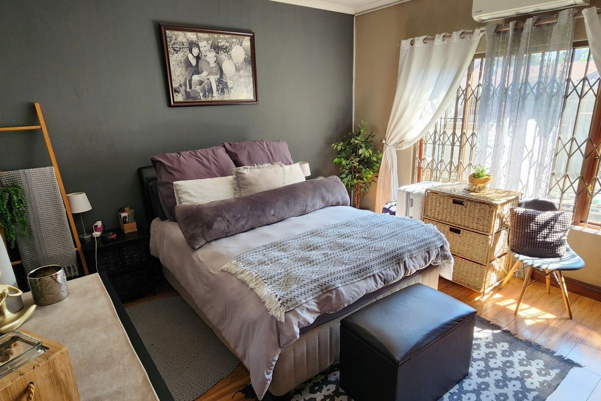 A well-maintained bedroom featuring laminate flooring, a security gate on the window, and an integrated air conditioning unit.