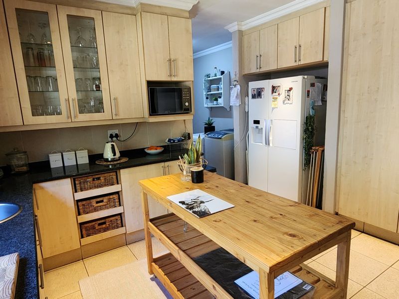 A functional kitchen featuring light wood cabinetry, granite countertops, a stainless steel sink, and ample storage space with a dedicated pantry cupboard.