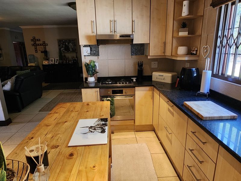 A functional kitchen featuring light wood cabinetry, dark granite countertops, a gas hob, and an integrated oven, with an open-plan flow to the living area.