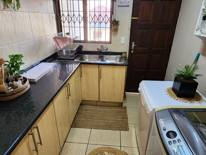 A functional laundry area featuring granite countertops, laminate cabinetry, a double sink, and tiled flooring with a secure exterior door.