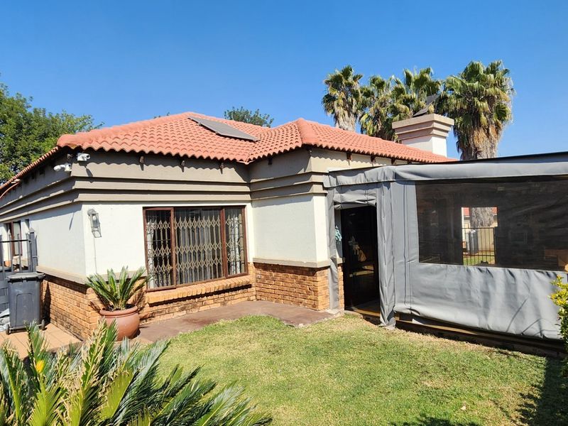 Rear view of the house featuring a terracotta tiled roof, brick and plaster facade, and an enclosed patio area overlooking the garden.