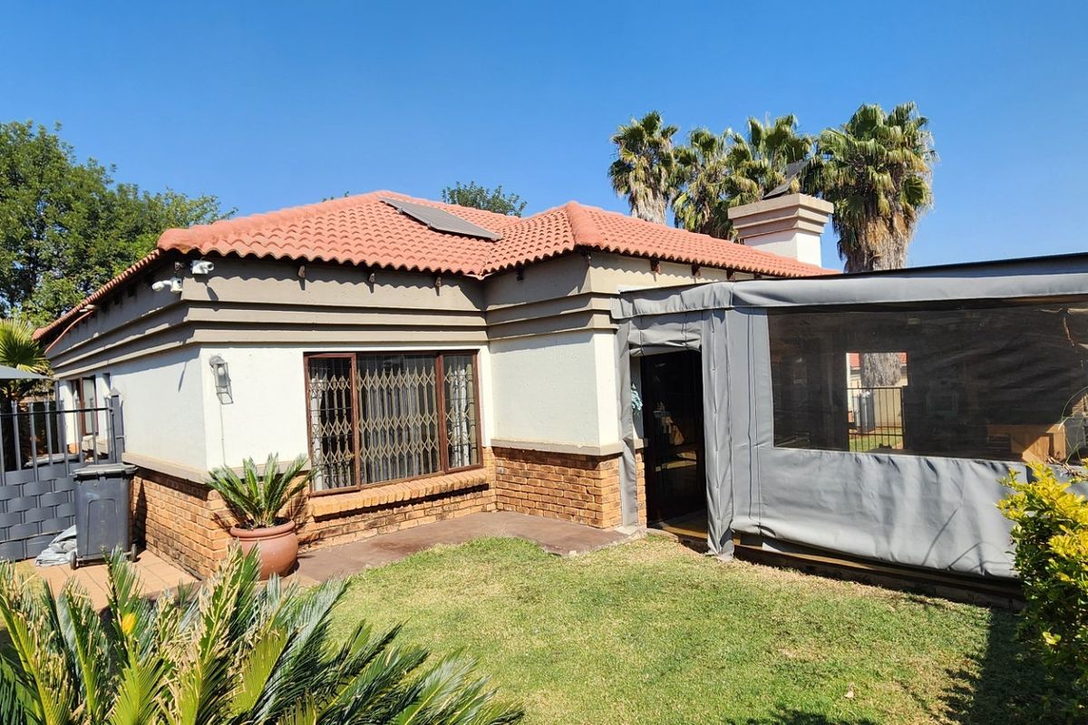 Rear view of the house featuring a terracotta tiled roof, brick and plaster facade, and an enclosed patio area overlooking the garden.