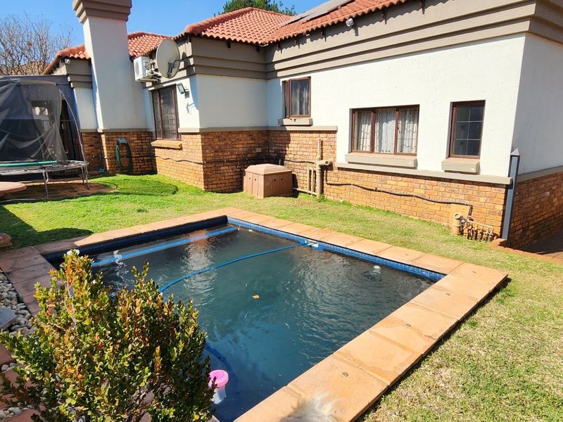 Rear garden area featuring a swimming pool with tiled coping, brick and plaster facade, and terracotta roof tiles.
