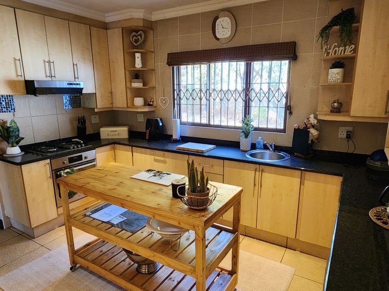 A functional kitchen featuring light wood cabinetry, granite countertops, a gas hob, and a stainless steel sink with a tiled splashback.