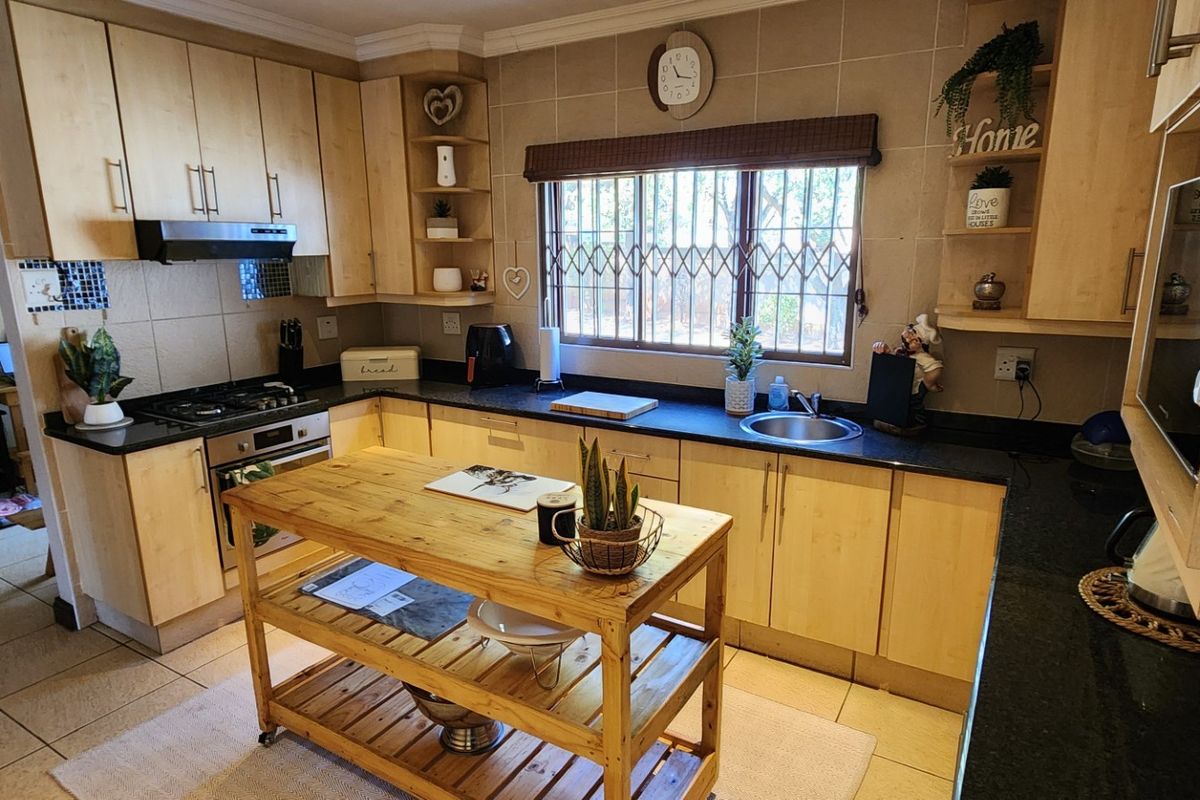 A functional kitchen featuring light wood cabinetry, granite countertops, a gas hob, and a stainless steel sink with a tiled splashback.
