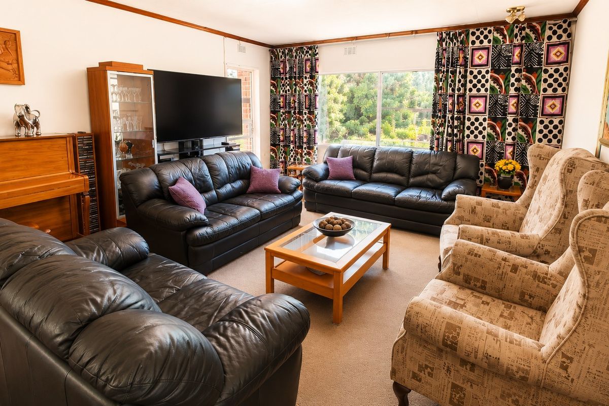 A spacious living room featuring large windows that provide natural light and views of the garden, finished with neutral carpeting.