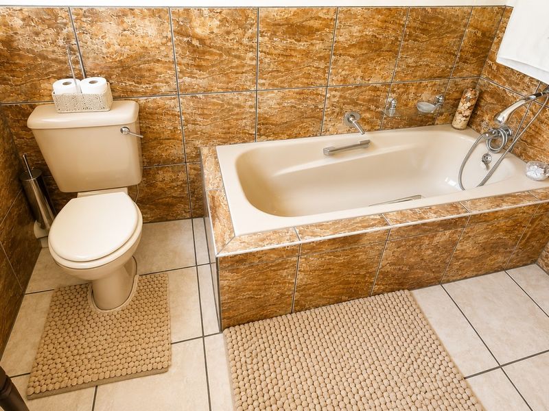 A functional bathroom featuring a built-in bathtub, toilet, and full-height decorative ceramic wall tiling.